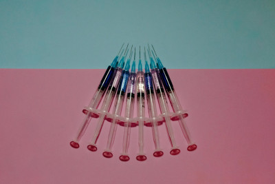 Several syringes arranged in a row on a pink and blue background.