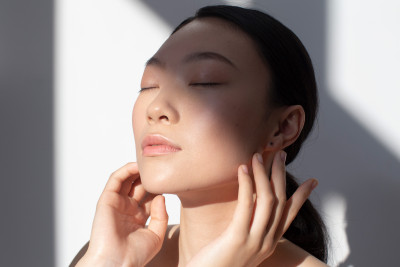 Nahaufnahme einer Frau mit makelloser Haut, geschlossenen Augen, genießt Sonnenlicht.